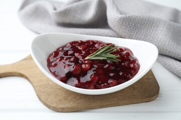 Fresh cranberry sauce and rosemary in bowl on white wooden table, closeup