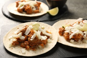 Delicious tacos with vegetables, meat and lime on grey table, closeup