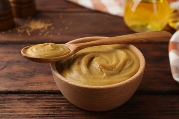 Bowl and spoon with tasty mustard sauce on wooden table, closeup