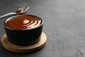 Tasty barbeque sauce in bowl on dark textured table, closeup. Space for text