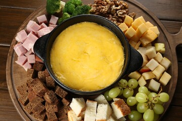 Fondue pot with melted cheese and different products on wooden table, top view