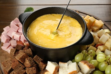 Fondue pot with melted cheese and different products on wooden table, closeup
