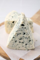 Wooden cutting board with blue cheese on white tiled table