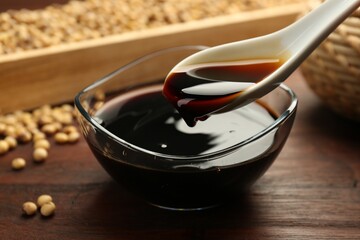 Taking soy sauce with spoon from bowl at wooden table, closeup