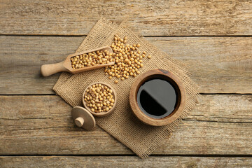 Soy sauce in bowl and soybeans on wooden table, flat lay