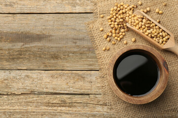 Soy sauce in bowl and soybeans on wooden table, flat lay. Space for text - obrazy, fototapety, plakaty