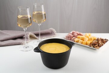 Fondue with tasty melted cheese, different products and aromatic wine in glasses on white table