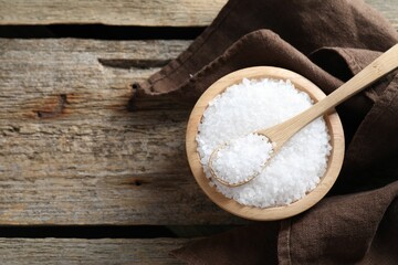 Organic salt in bowl and spoon on wooden table, top view. Space for text
