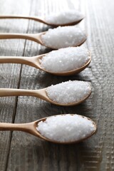 Organic salt in spoons on wooden table, closeup