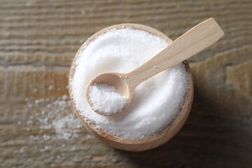 Organic salt in bowl and spoon on wooden table, top view
