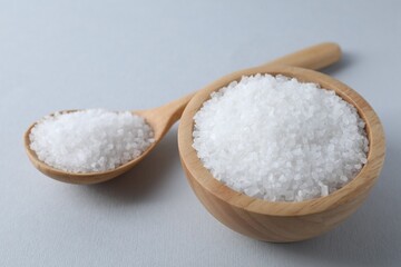 Fototapeta na wymiar Organic white salt in bowl and spoon on light grey background, closeup