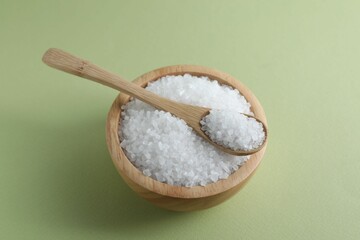 Organic white salt in bowl and spoon on olive background, above view