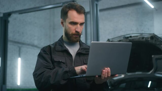 Caucasian man auto mechanic in repair shop using laptop technology electronic car maintenance male expert service manager use device computer diagnostics of fixing vehicle in garage vehicle station