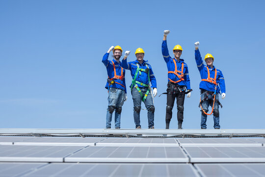 Engineers raised their fist up on solar panels against blue sky  after finish their work