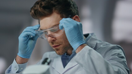 Naklejka premium Scientist wearing safety glasses investigate medicines in laboratory close up.