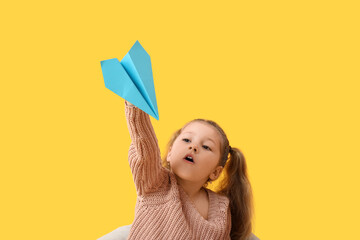 Cute little girl with paper plane on yellow background