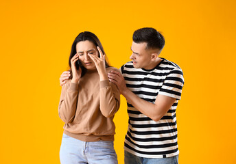 Upset young woman talking by mobile phone and her husband on yellow background