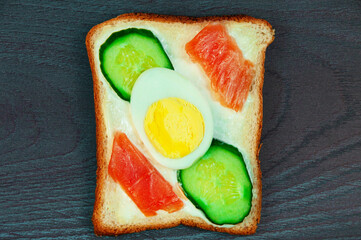 a slice of bread with boiled egg, cucumber and red fish. appetizing sandwich with vegetables and...