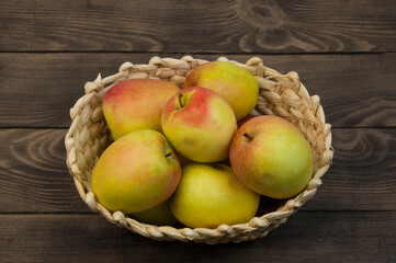 redsided apples in a wicker basket on a wooden background. sweet yellow apples on a brown texture