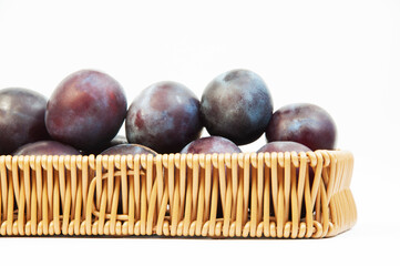 round blue plums in a basket on a white background. ripe sweet plums on a light texture