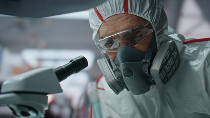 Biochemistry specialist looking microscope in decontamination suit lab close up