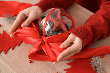 Woman tying bow on Christmas ball at wooden table
