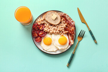 Plate with tasty English breakfast and glass of juice on turquoise background