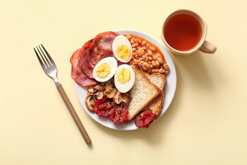 Fototapeta na wymiar Plate with tasty English breakfast and cup of tea on yellow background