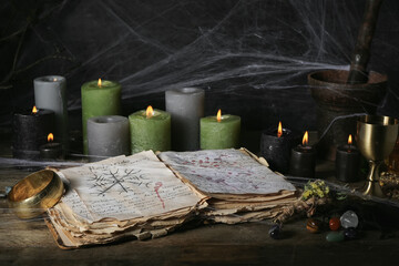 Witch's magic attributes with spell book and burning candles on dark wooden table