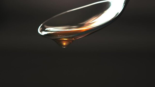 Cuchara vertiendo miel con fondo negro. L&iacute;quido marr&oacute;n viscoso que cae suavemente. Textura liquida espesa. Macro. 4k 60fps