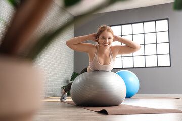 Beautiful young woman in sportswear exercising on fitness ball at gym