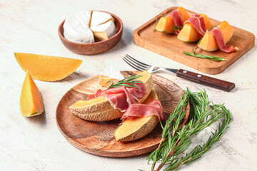 Plate with tasty melon, prosciutto, rosemary and cheese on light background
