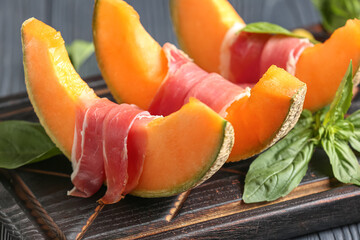 Wooden board with tasty melon, prosciutto and basil, closeup