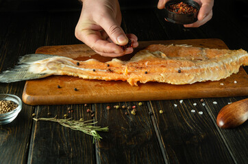 The cook prepares fresh raw fish on a wooden cutting board. Homemade delicious fish dish according to an old recipe with aromatic spices