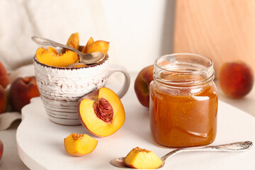 Jar with sweet peach jam and cup of fresh fruits on table