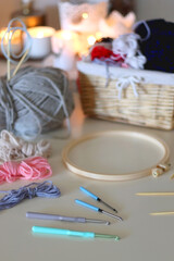 Balls of yarn, threads, various needlecraft needles and lit candles on the table. Hygge at home. Selective focus.