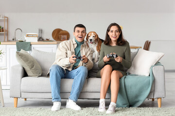 Young couple with cute Beagle dog playing video game at home