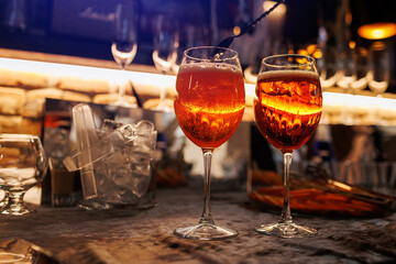 Two glasses of cocktail Aperol spritz on bar counter. Making typical alcoholic italian beverage, aperitif made with Prosecco sparkling white wine, ice and fresh orange slices. Mixing orange liquid.