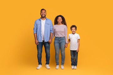 Smiling black family with preteen son holding hands while posing together