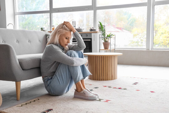 Depressed mature woman sitting on floor at home