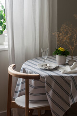 A cozy corner of the living room - a table set for dinner with a tablecloth and dishes, a chair