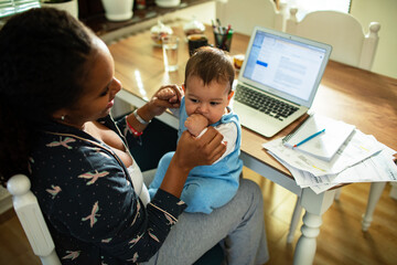 Multitasking mother holding baby while working from home