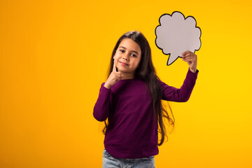 Thoughtful kid girl holding cloud bubble card over yellow background. Dreaming concept