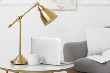 Laptop with cup and lamp on table in light living room