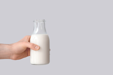 Hand with bottle of milk on grey background