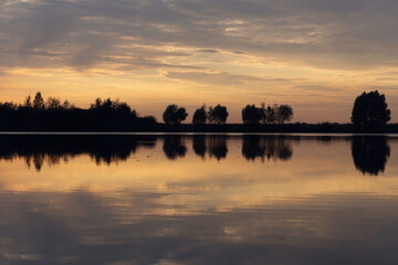 View of the lake in twilight. Sunset, warm colors. Calm water reflecting clouds.