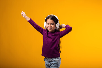 Smiling kid girl enjoying music in headphones on yellow background. Lifestyle and leasure concept