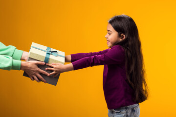 Smiling kid girl accepting gift box over yellow background. Birthday and celebration concept