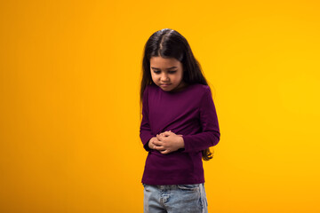 Little girl feeling abdominal pain, keeping hands on stomach because indigestion, painful illness...
