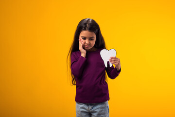 Girl holding papercraft tooth and touching mouth with hand with painful expression because of toothache or dental illness on teeth. Dentist concept.